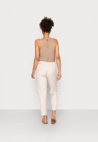 Body côtelé marron avec dos en trou de serrure, associé à un pantalon fuselé beige clair, complété par des sandales plates marron clair.