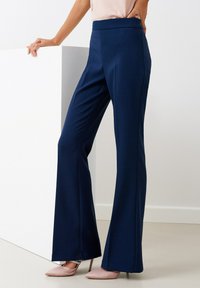 Pantalones de pierna ancha en navy con una textura suave, cintura alta y sin cierres visibles, combinados con tacones de punta rosa claro.