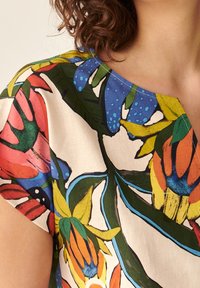 Blomstret bluse med rund halsudskæring, der har levende farver som rød, blå, gul og grøn, på en lys baggrund, der fremhæver markante bladmønstre.