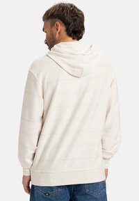 Lys beige hoodie med et tekstureret stof. Har horisontale striber i en subtil lyserød kontrast. Kommer med en stor hætte og lange ærmer.