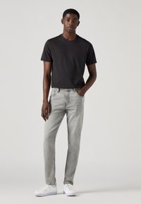 Tricou negru cu mânecă scurtă, blugi din denim gri și adidași albi. Ținuta are un design simplu, ajustat, cu detalii clasice de cusătură.