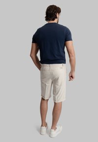 T-shirt blu navy a maniche corte abbinato a pantaloni beige con righe verticali, tasche posteriori e sneakers bianche.