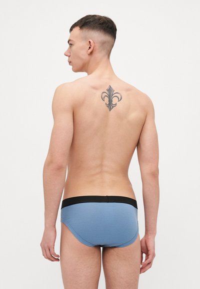 Culotte pour homme de couleur bleu clair avec une taille noire, dotée d'un ajustement serré et d'un design minimaliste. La vue arrière met en avant un tatouage sur le haut du dos.