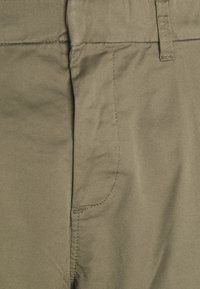 Pantaloni di cotone verde oliva con cuciture visibili, due tasche frontali e una texture liscia. Design a gamba dritta e vita classica.