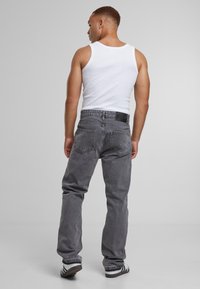 Jean en denim gris à coupe décontractée, avec deux poches arrière et une ceinture noire simple, associé à un débardeur blanc.