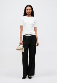 Biela krátka manga tričko, čierne nohavice s širokými nohavicami a čierne lodičky. Outfit dopĺňa béžová kabelka s podpisovým akcentom.