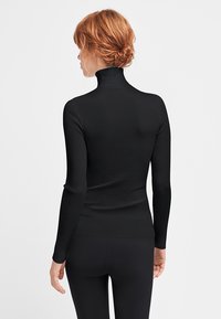Schwarzer gerippter Rollkragenpullover mit langen Ärmeln, figurbetonter Silhouette und weichem Material. Die Rückansicht zeigt den hohen Kragen und glatte Nähte.