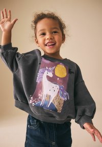 Sudadera gris con un diseño de unicornio con detalles en púrpura y dorado, combinada con jeans azul oscuro. Material texturizado y ajuste relajado.