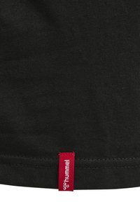 Czarna bawełniana koszulka z płaskim dołem, z małą czerwoną naszywką z logo "hummel" przeszytą w prawym dolnym rogu.