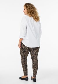 Hvid skjorte med knaplukning og oprullede ærmer, parret med leggings i sort og tan leopardprint og sorte flade sko. Glat stoftekstur.
