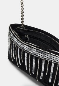 Sort ruskinds clutch-taske med sølvfarvet paillet-bolde, kædestrop, lynlås-lukning og indvendig lomme til sikker opbevaring.