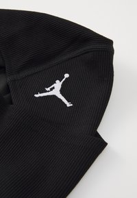 Sort strikket hat med et hvidt Jumpman-logo. Teksturen er ribbet, og designet har en tætsiddende form med en buet kant.