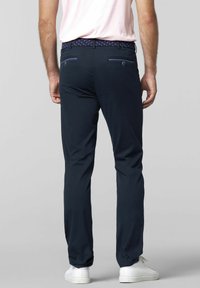 Marineblauwe broek met een slim fit, een gestructureerde tailleband, twee achterzakken met contrasterende rand, en gecombineerd met witte schoenen.