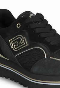 Sneaker nera con un tessuto testurizzato e una parte superiore in suede liscio. Presenta dettagli del logo metallici, strisce a contrasto e una suola in gomma spessa.