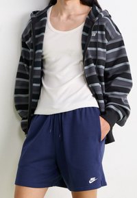 Černobíle pruhovaná zipová mikina s bílým tílkem a námořnickými šortkami. Na šortkách je logo Nike. Měkký materiál s volným střihem.