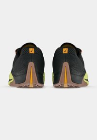 Ζευγάρι μαύρων και κίτρινων αθλητικών παπουτσιών που βλέπεται από τη φτέρνα, δείχνοντας τις υφασμάτινες σόλες και τα λογότυπα της Nike στις ταμπέλες της φτέρνας.