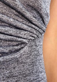 Tessuto grigio con texture e dettaglio arricciato, che mostra un primo piano di un materiale morbido e elastico. La superficie presenta un delicato motivo melangiato.