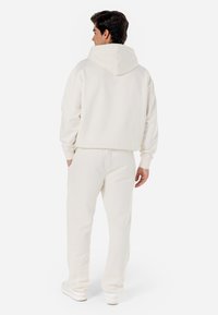 Sweat à capuche blanche avec une grande capuche, des poignets côtelés et un pantalon de jogging assorti, fabriqués en tissu doux, avec une coupe décontractée et un design minimal.