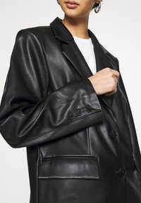 Sort læderjakke med notched lapel, fire knapper foran og to forlommer, med glat tekstur og skræddersyet pasform.