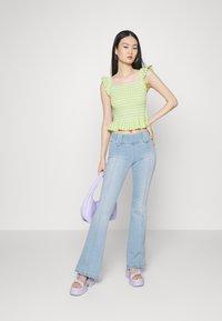 Top cropped em gingham verde com mangas com babados, combinado com jeans claros de corte evasê. Acessórios incluem uma bolsa lavanda e sapatos de plataforma.