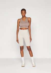 Športová podprsenka z ľahko hnedého materiálu s priliehavým strihom, doplnená béžovými cyklistickými šortkami s vysokým pásom, bielymi teniskami a ponožkami.