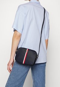 Navy Crossbody-Tasche mit rot-weißen Streifen, aus glattem synthetischen Material, quadratischer Form, silberner Hardware und verstellbarem Griff.