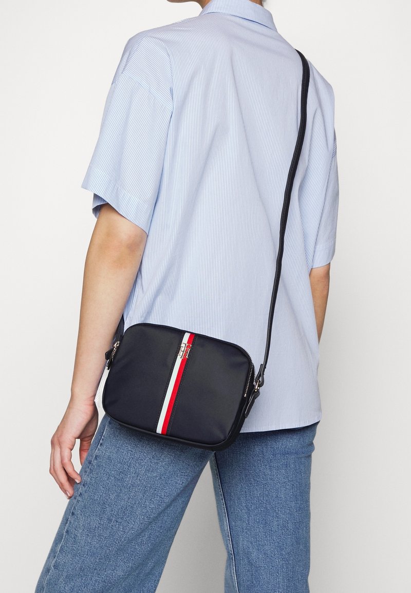 Navy Crossbody-Tasche mit rot-weißen Streifen, aus glattem synthetischen Material, quadratischer Form, silberner Hardware und verstellbarem Griff.