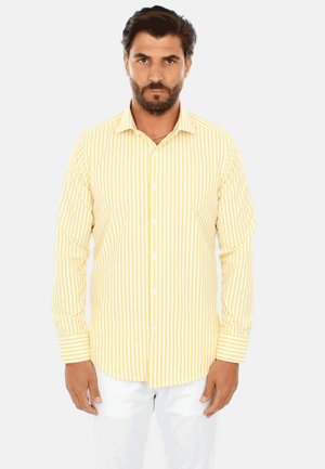Camicia a maniche lunghe a righe gialle e bianche con chiusura a bottoni, colletto standard e maniche con polsino. Il tessuto sembra morbido e liscio.