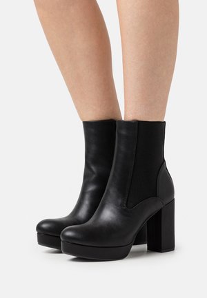 Bottes basses en cuir noir avec un design élégant, dotées de panneaux latéraux élastiques et d'un talon bloc épais. Texture lisse, forme moderne.