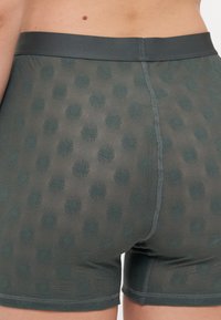 Shorts boxers de couleur vert foncé, fabriqués dans un matériau texturé, avec un motif floral répétitif et une ceinture lisse.