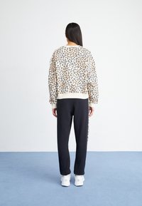 Felpa a stampa leopardata in crema con dettagli neri, abbinata a pantaloni tuta neri. Composizione in misto cotone, vestibilità rilassata, polsini e orlo a costine.