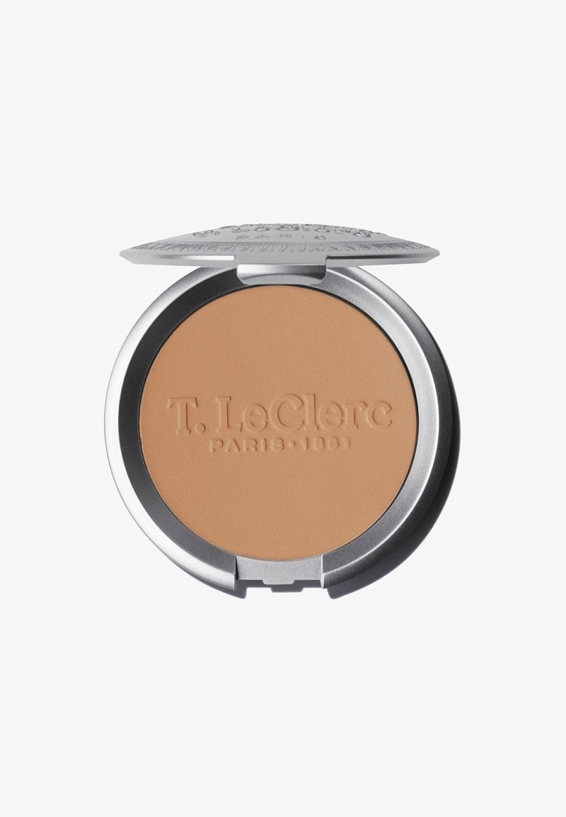 Kompaktpuder in einer runden silbernen Dose, mit einer matten beigen Oberfläche und eingeprägtem Markennamen. Der Deckel öffnet sich mit einem Scharnier für einen einfachen Zugang.