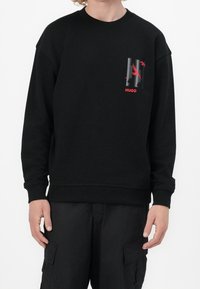 Felpa nera con maniche raglan, polsini e orlo a costine. Presenta un logo grafico rosso e dettagli sulla tasca del petto. Tessuto con una texture morbida.
