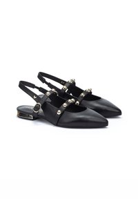 Zapatos de cuero negro tipo slingback con punteras puntiagudas, que cuentan con tachuelas en tono dorado a lo largo de las correas y un pequeño tacón decorativo.