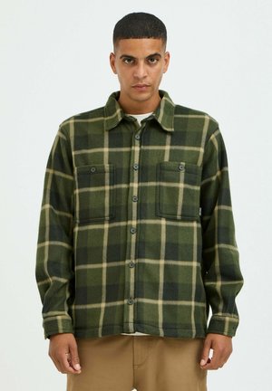 Camicia in flanella a quadri verde e crema con chiusura a bottoni, due tasche sul petto e colletto piegato. Maniche lunghe con polsini a bottoni.