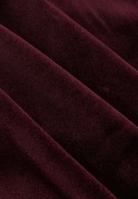 Tessuto bordeaux con una superficie morbida e testurizzata, caratterizzato da un sottile lucido e da pieghe stratificate che creano profondità.