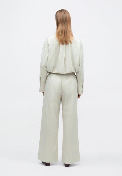 Chemise gris clair, ample, et pantalons à jambes larges. Présente un froncé à l'arrière, des poignets à boutons et une texture douce.