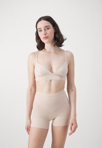 Light beige seamless bralette with adjustable straps and matching high-waisted shorts. Smooth texture, minimalist design, fitted shape.
