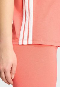 Koral atletisk topp med tre hvite striper på siden, kombinert med matchende koral leggings. Myk, elastisk bomullsmateriale.