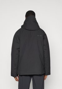 Czarna ocieplana kurtka z kapturem, o gładkiej fakturze i minimalistycznym wzornictwie. Z tyłu przy ramieniu widoczny detal z logo.