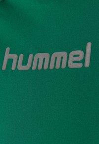 Grüner Stoff mit glatter Textur, der das Wort "hummel" in hellgrauer, moderner Schriftart zeigt, zentral angeordnet.