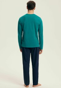 Turkusowa koszula z długim rękawem zestawiona z granatowymi spodniami. Koszula ma okrągły dekolt i gładką fakturę. Oba elementy odzieży mają luźny krój.