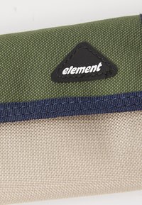 Zelená látková peňaženka s béžovým dnom, vystuženým modrým prešívaním a čiernou trojuholníkovou nášivkou s nápisom "element."