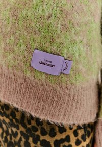 Sweter o puszystej fakturze, w odcieniach jasnej zieleni i bladego różu, z dolną częścią w panterkę. Metka nosi napis "Naoko Knitwear".