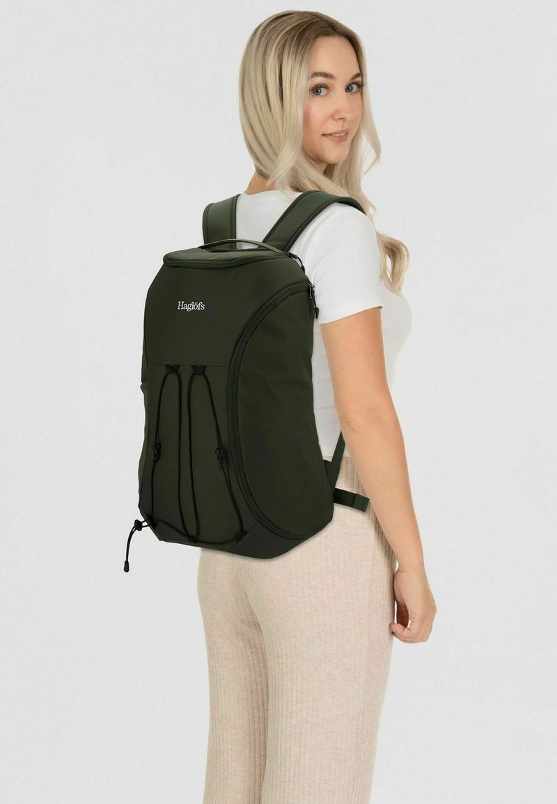 Dunkelgrüner Rucksack mit gepolsterten Trägern, abgerundetem Oberteil und externem Bungee-Seil. Mit Logo auf der Vorderseite und zwei Seitentaschen.