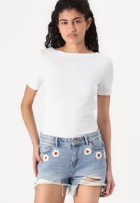 T-shirt blanc à manches courtes associé à un short en denim déchiré orné de fleurs brodées en orange et blanc.
