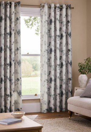 Floor-length light curtains with black and gray floral print hanging on a metal rod over a window in a beige living room.