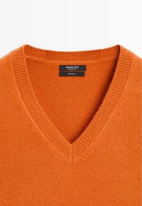 Orange wool sweater with a V-neck design, featuring ribbed edges and a sewn-in label displaying brand and material information.