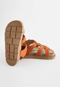 Orangemockasinsandas med flera korsade remmar, en texturerad gummisula och en vadderad fotbädd med en färgglad design.