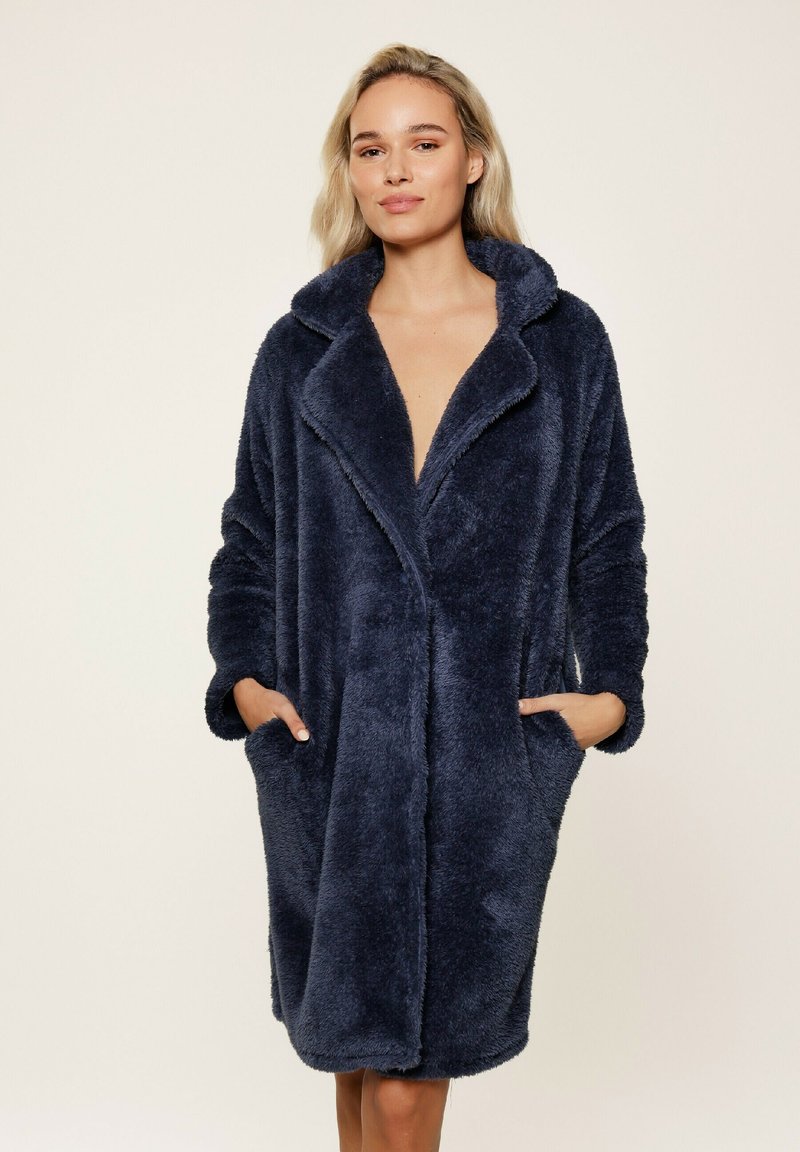 Accappatoio oversized, di colore blu navy, in morbido tessuto con collo a scialle, maniche lunghe e tasche laterali, caratterizzato da una finitura in tessuto soft e testurizzato.